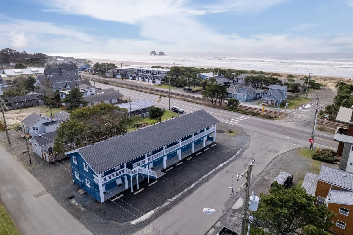 This image captures the vibrant blue building with an ocean view in the background, surrounded by neighboring houses and a road leading directly to the beach. The scene exudes a relaxed mood, with the beach just steps away and the convenience of community life evident.