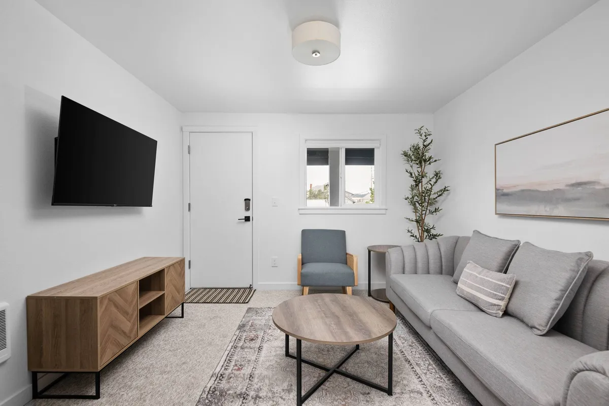 This image features a cozy and inviting living area with a plush sofa, coffee table, TV, tasteful artwork on the wall, and a leafy plant adding a touch of nature. The scene communicates comfort and relaxation, with ample seating for unwinding after a day at the beach.