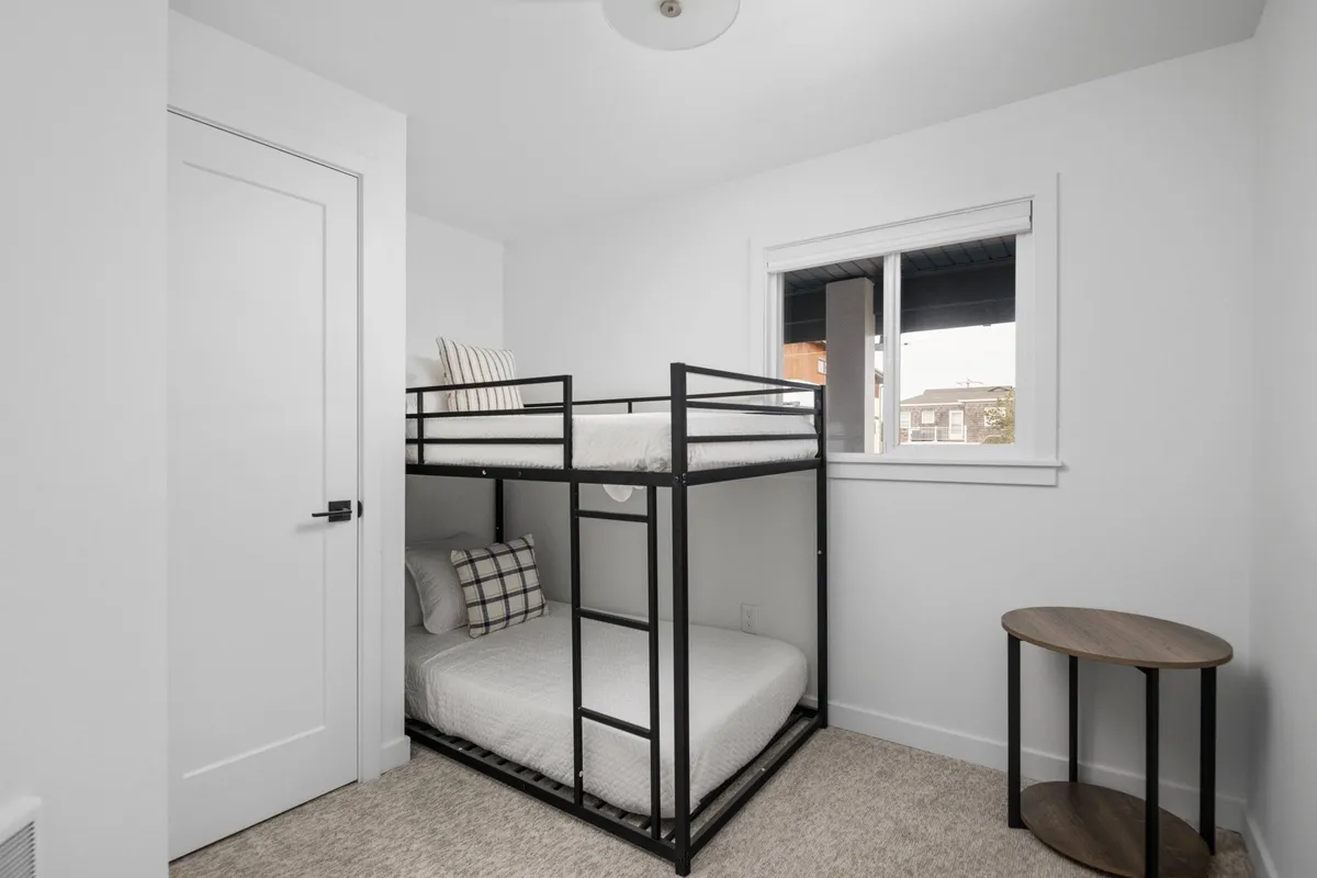 A warm, inviting nook featuring a set of bunk beds fitted with soft bedding. A window provides daylight, while a small side table and reading lamp add functional charm. The space strikes a balance between playfulness and comfort, appealing to families or groups.