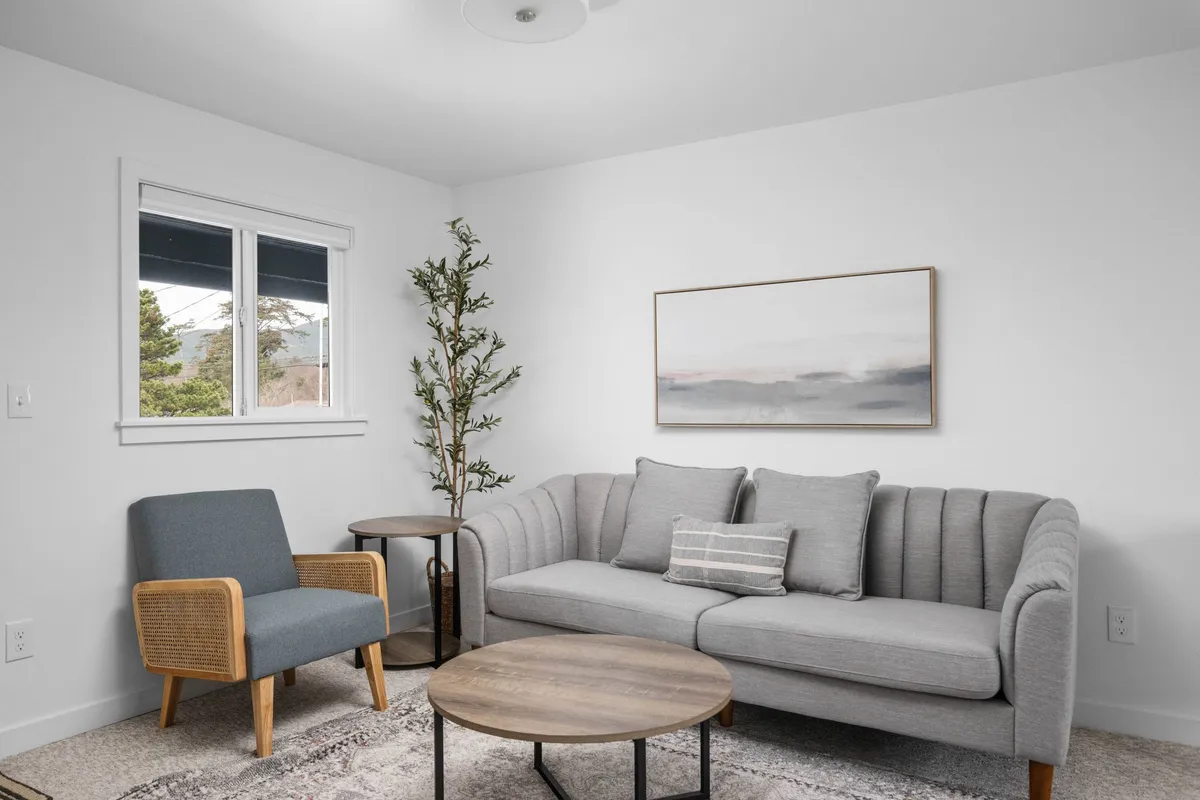 This interior shot highlights a harmonious and comfortable lounge space with a sofa, an armchair, a neat coffee table, wall art, and an indoor plant. Sunlight streams in, suggesting a bright and welcoming atmosphere ideal for reading or socializing.